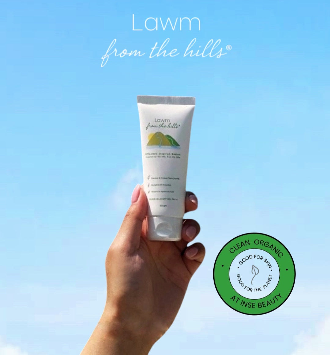 Hand holding a tube of 'Lawm from the Hills' against a clear blue sky with a green logo at the bottom right corner.